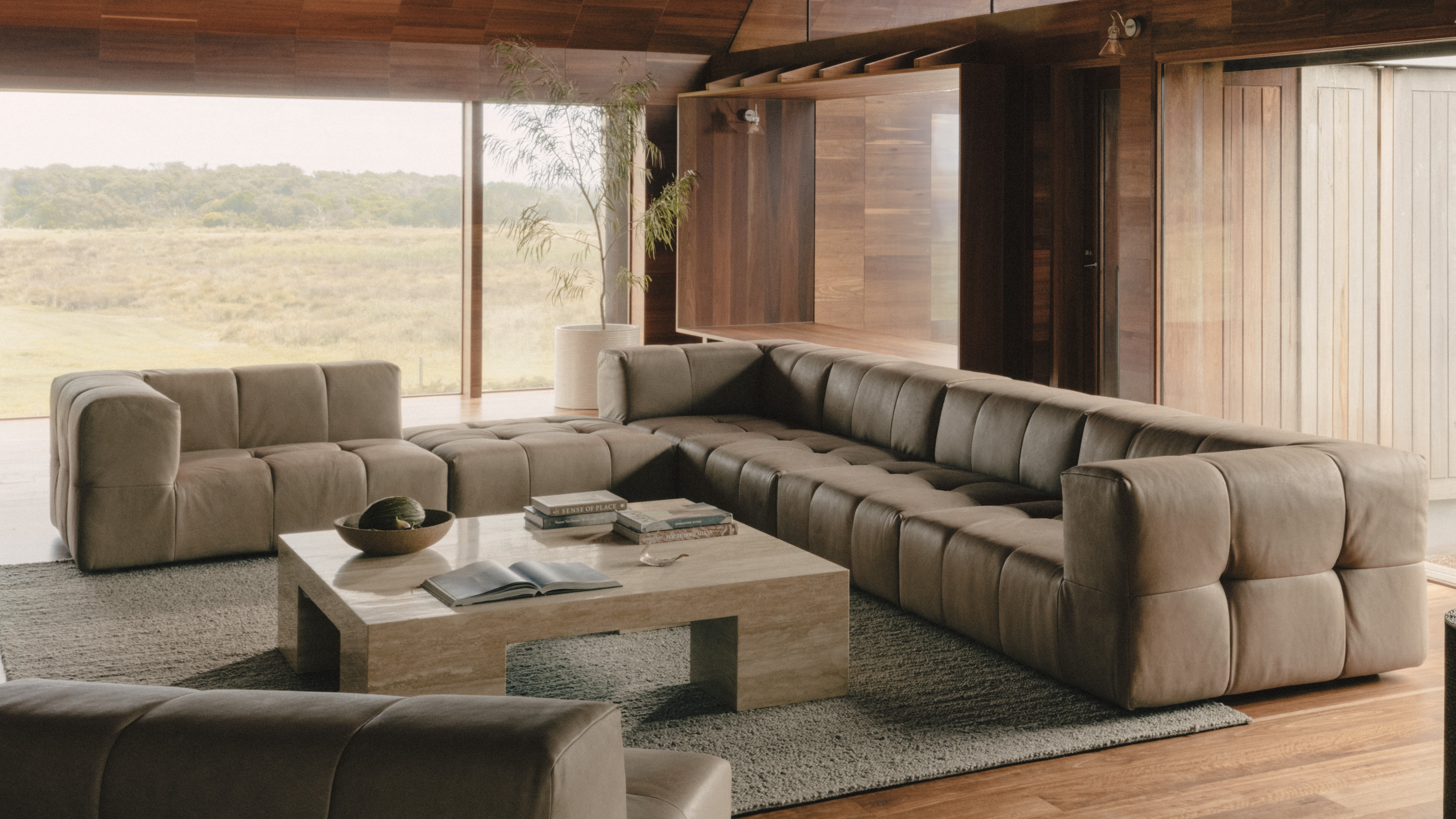 Coco Republic Omega Modular Sofa in taupe velvet, styled in a timber-lined living room with panoramic windows and a stone 