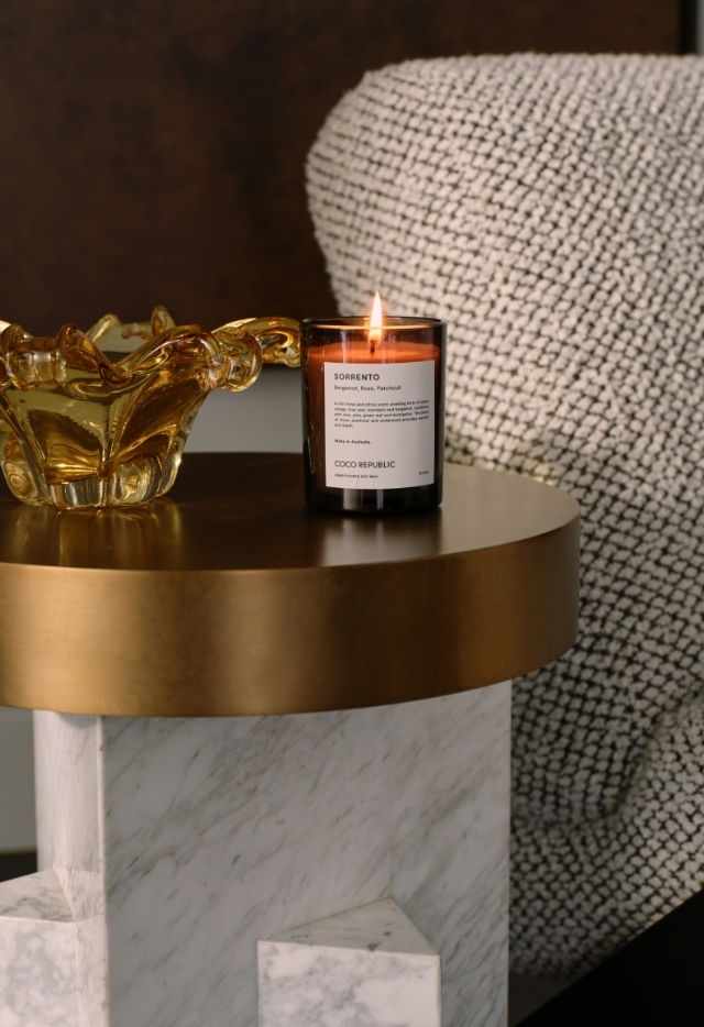 Detail of marble and brass side table styled with a lit candle and amber glass decor piece