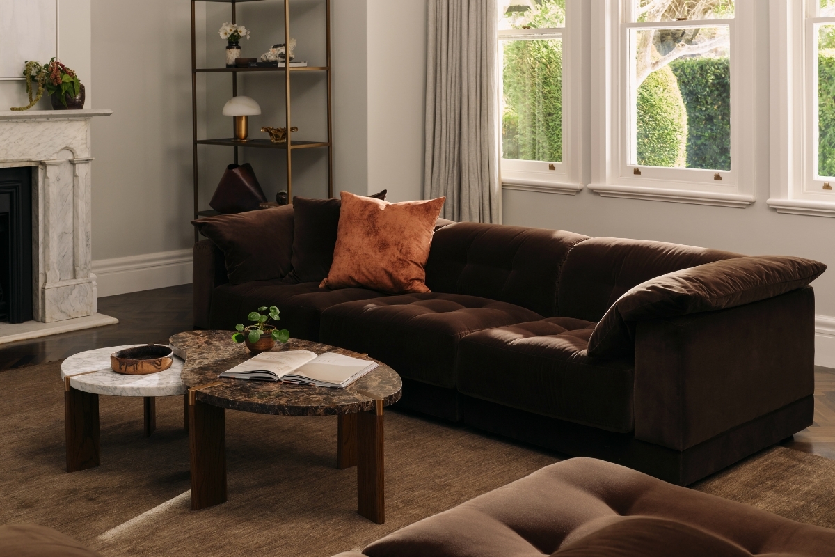 Moody living room with chocolate velvet sofa, nested marble coffee tables and warm neutral accents