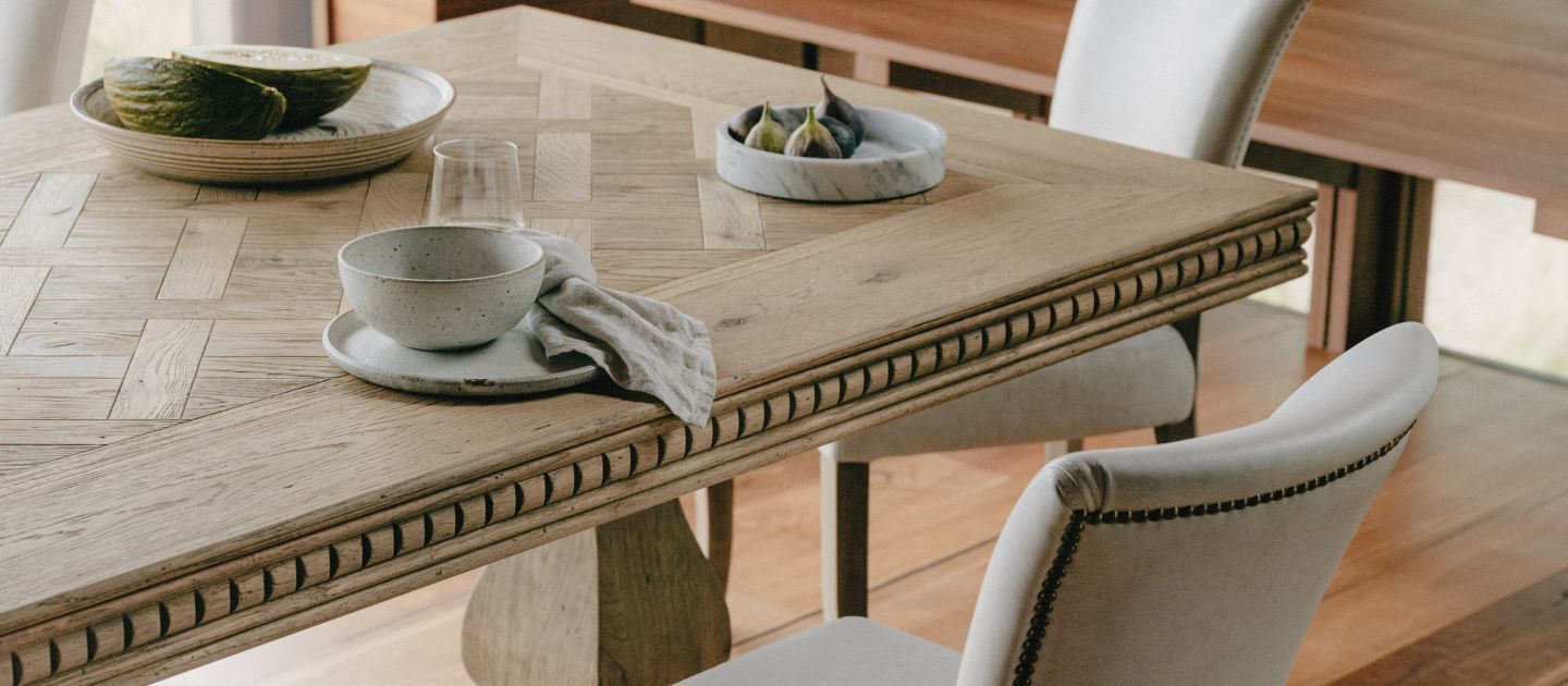 A parquetry timber dining table laid with various plates and bowls