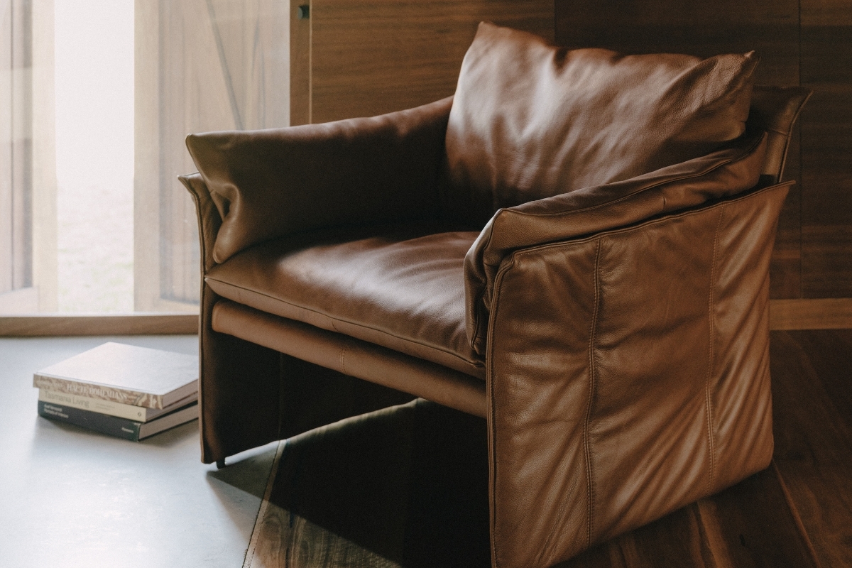 Vintage-inspired leather occasional chair with relaxed cushioning and exposed stitching, set beside timber panelling and filtered natural light