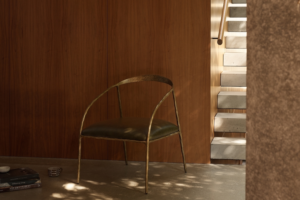 Minimalist mid-century style chair with hammered brass frame and black seat, styled in a quiet architectural corner with natural shadow play