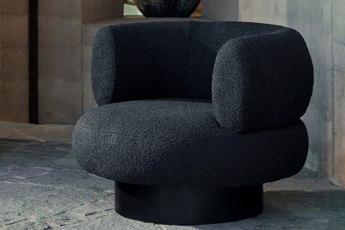 Sculptural black boucle swivel chair with rounded back and concealed base in a stone architectural setting