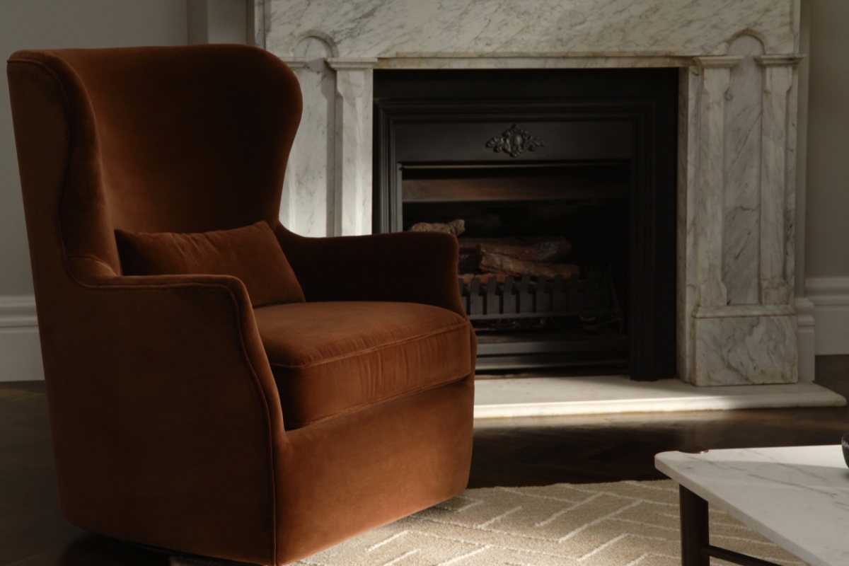 Deep burnt orange velvet, softly curved, high-back chair styled beside marble fireplace and tonal rug in a quiet reading space