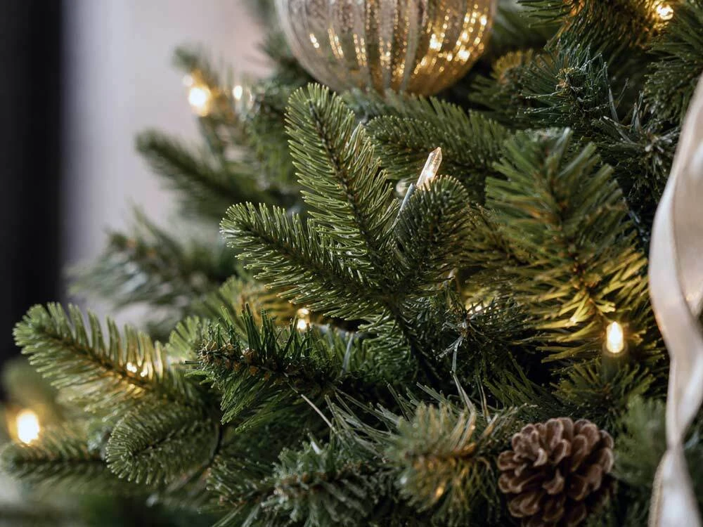 Close-up of realistic artificial Christmas tree foliage, branch tips, lights and pinecone detail