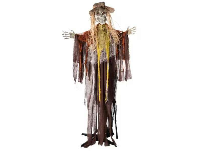 A spooky Halloween decoration of a scarecrow with a skull face, glowing red eyes, tattered brown and orange clothing, and straw accents.