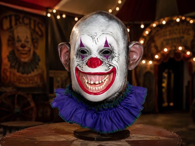 Circus Crazy Ape latex clown mask displayed on a stand in a vintage carnival sideshow scene