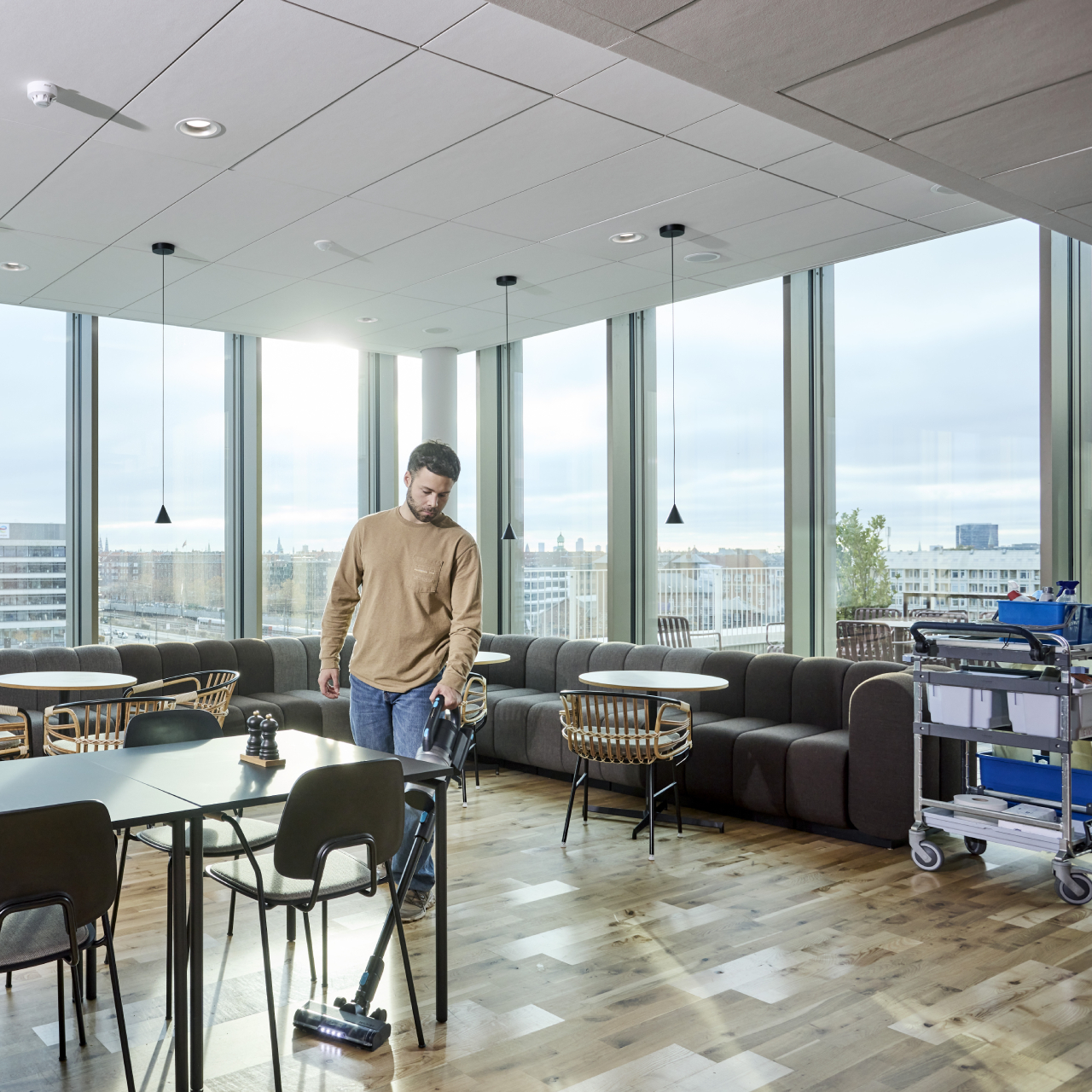 Nilfisk Advance VU200 cordless stick vacuum cleaning around tables in cafeteria