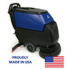 A digital photograph of the Pacific S-24XM Disk Walk-Behind Auto Scrubber, showing its compact and professional blue and black design with front-mounted scrubbing heads and rear squeegee assembly. The image includes a "Proudly Made in USA" label and American flag in the upper right corner, against a clean white background.