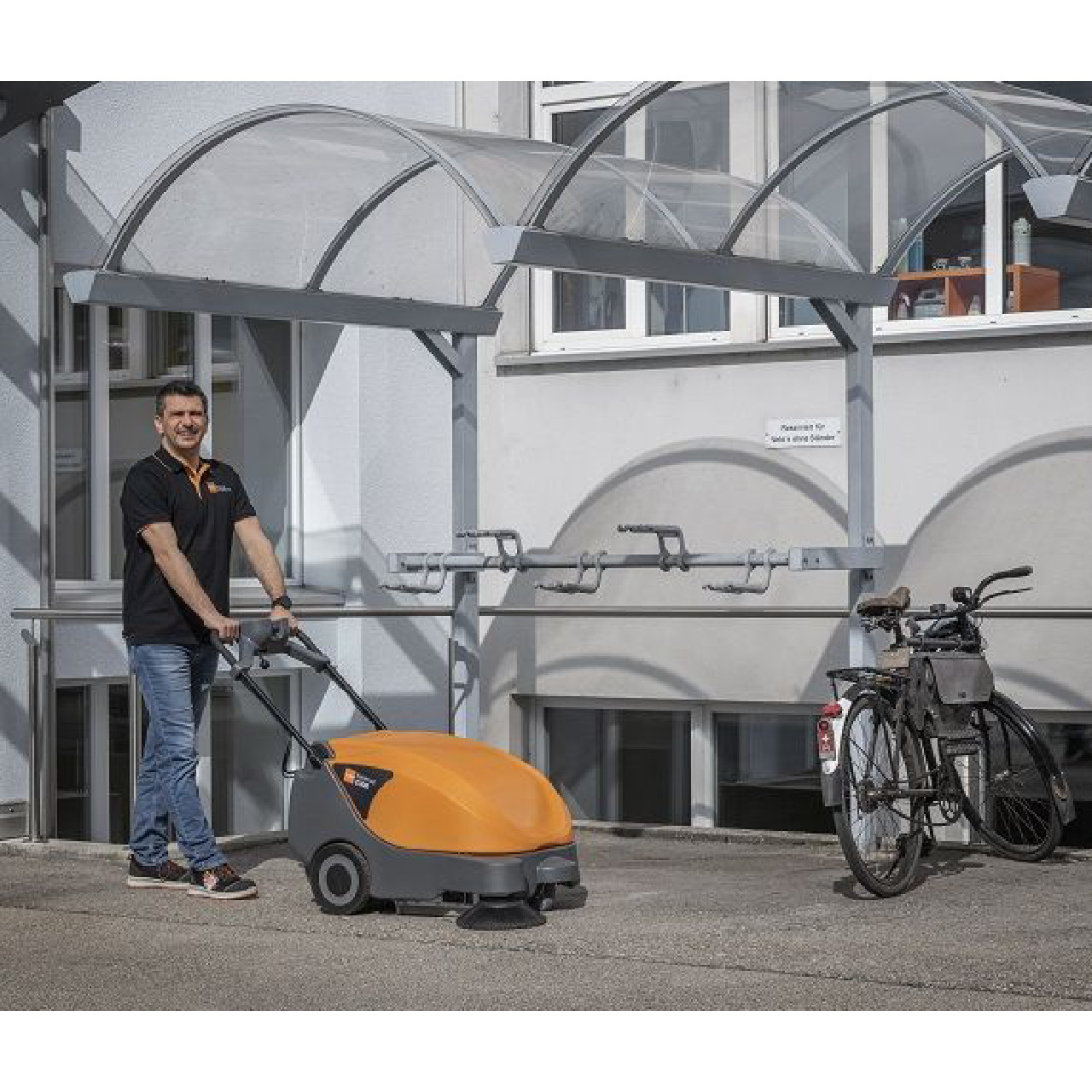 TASKI balimat 2300 commercial sweeper cleaning outdoor facility near bike rack and entrance