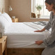 white-9-inch-deep-quilted-waterproof-fitted-mattress-protector-hand-demonstrating-elasticated-fit-quilted-texture-bedroom-lifestyle