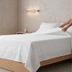 white-130-thread-count-cotton-rich-institutional-flat-sheet-on-bed-hand-demonstrating-durability-institutional-bedroom-setting