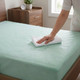 green-tint-waterproof-flame-retardant-mattress-protector-on-mattress-hand-demonstrating-water-resistant-properties-water-beading-off-surface