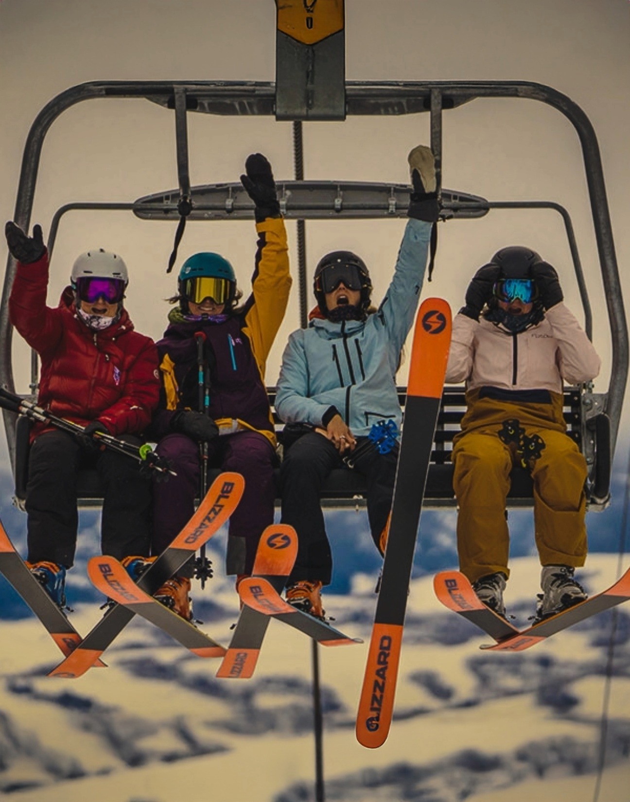 Four women on a chair lift with blizzard skis on.