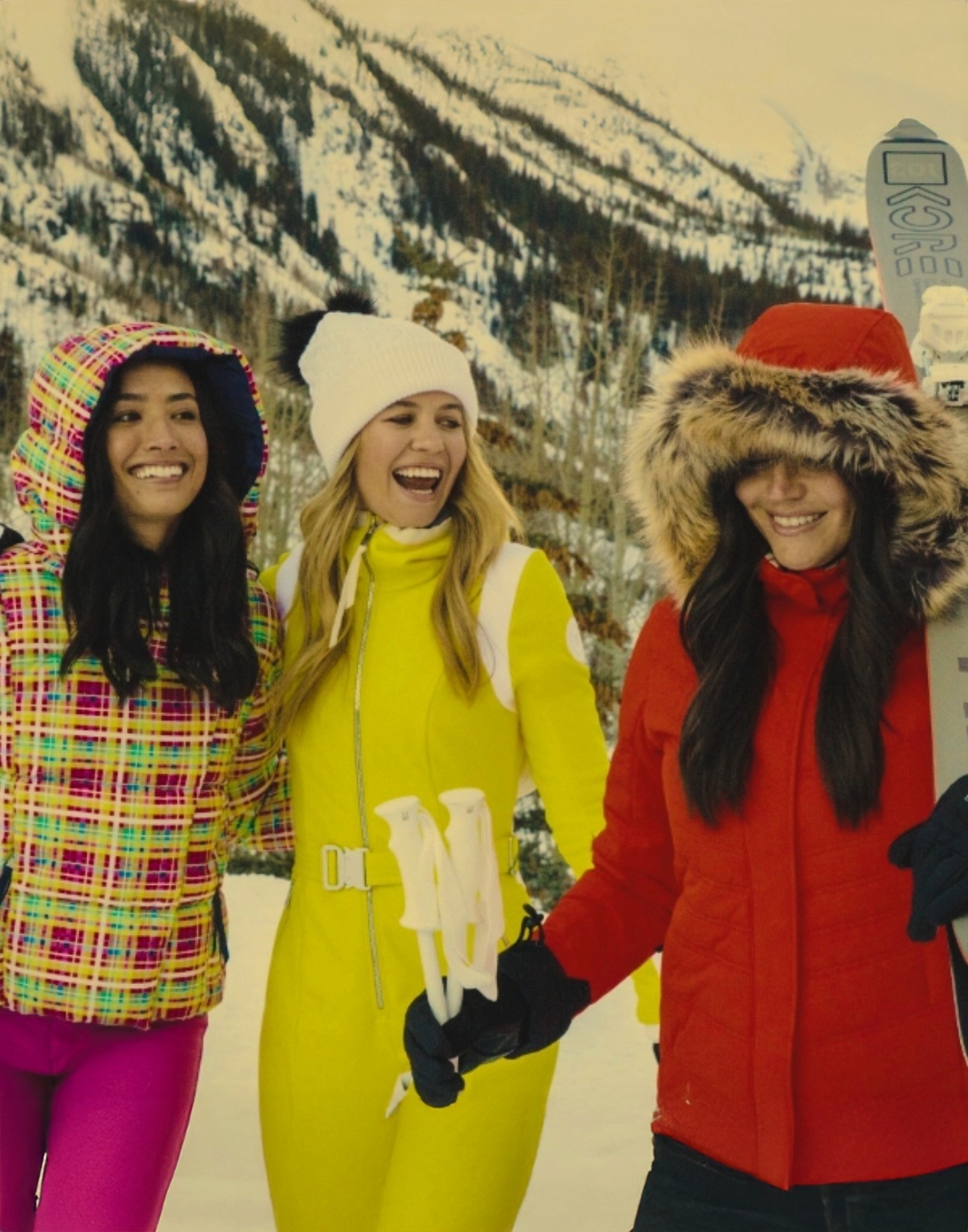 Three women wearing Obermeyer ski jackets carrying women's skis and poles.