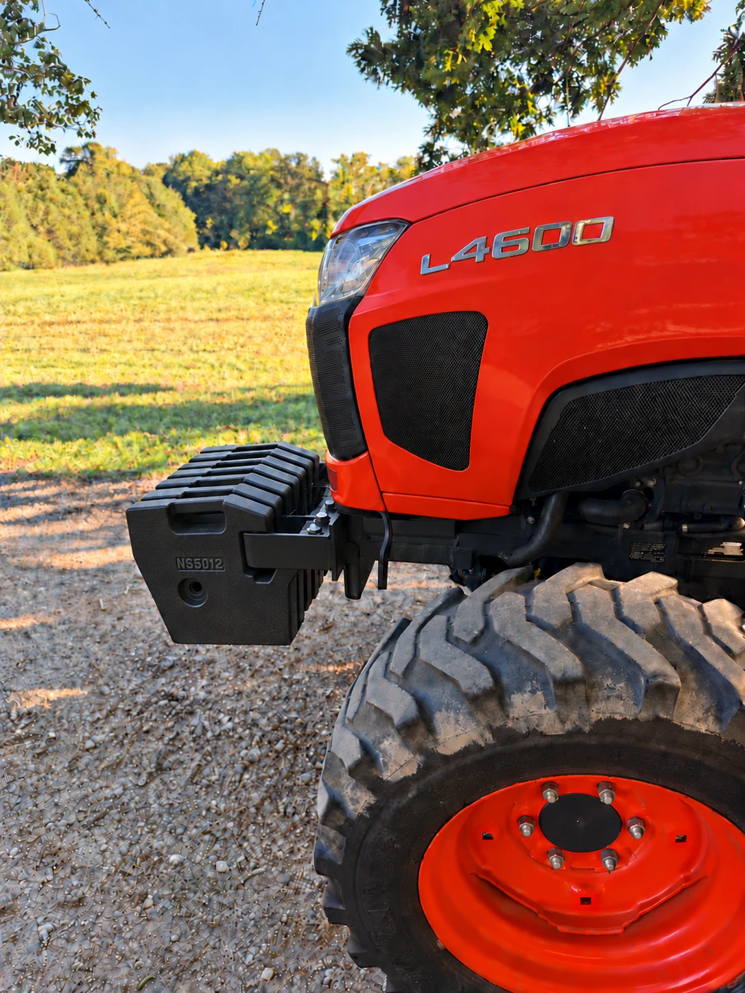 Orange L4600 tractor with black front suitcase weights beside a field