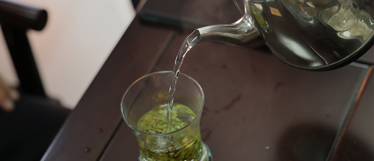 Hot water being poured into loose leaf tea in a cup