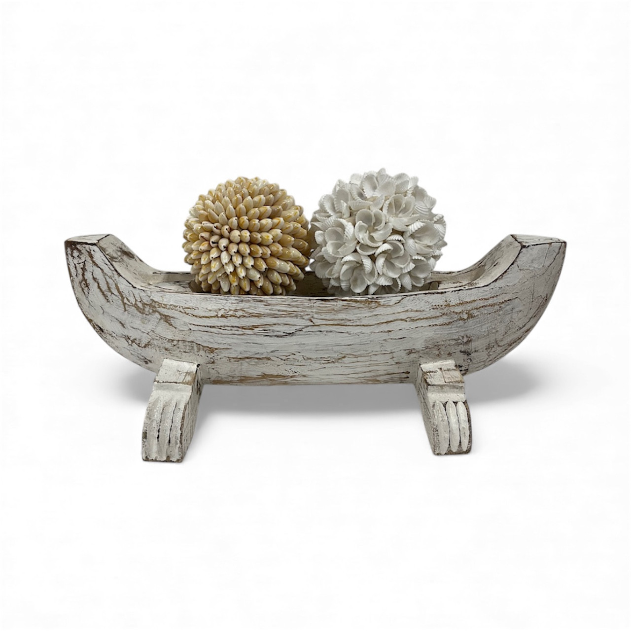A whitewashed wooden bowl resembling a fishing boat, with intricate carvings, adds a coastal vibe and rustic charm to any room's decor as a unique centerpiece.
