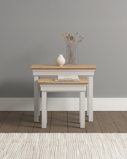 Vermont Nest of 2 Tables, product image of a set of ivory and oak nesting tables with one smaller table placed inside a larger table, decorated with a vase and a clear glass vase with dried plants.