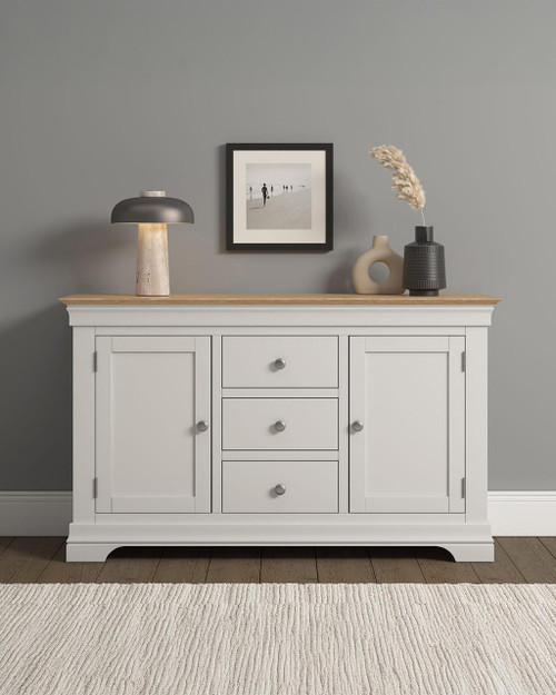 Vermont 2 Door 3 Drawer Sideboard in Ivory and Oak, featuring a natural wood top surface, with decorative vases and a lamp, against a modern gray wall.