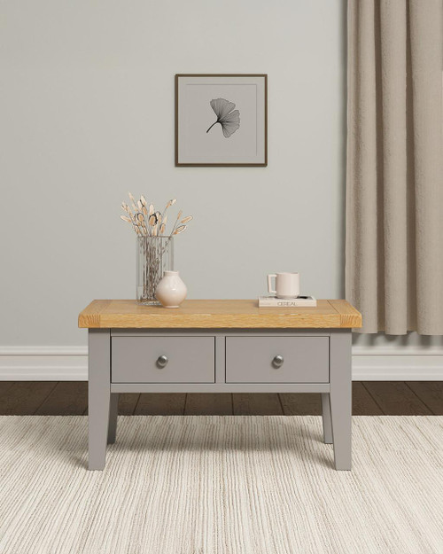 Hampton Pebble Grey 2 Drawer Coffee Table HG300-301-089, wooden coffee table with two drawers, grey painted finish and natural wood top, decorative vases and books on top, situated in a minimalist living space.