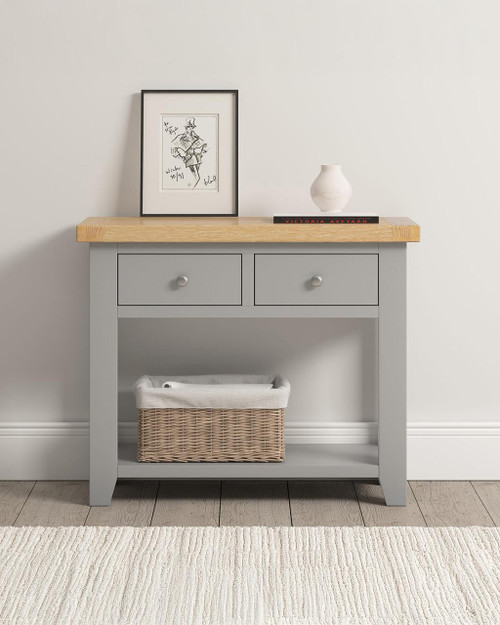 Hampton Pebble Grey 2 Drawer Console Table HG300-304-034, modern grey wooden console table with natural wood top, two drawers with round knobs, and a lower shelf with a wicker basket, minimalist decor with framed artwork and a vase. Hampton Pebble Grey 2 Drawer Console Table HG300-304-034, modern grey wooden console table with natural wood top, two drawers with round knobs, and a lower shelf with a wicker basket, minimalist decor with framed artwork and a vase.