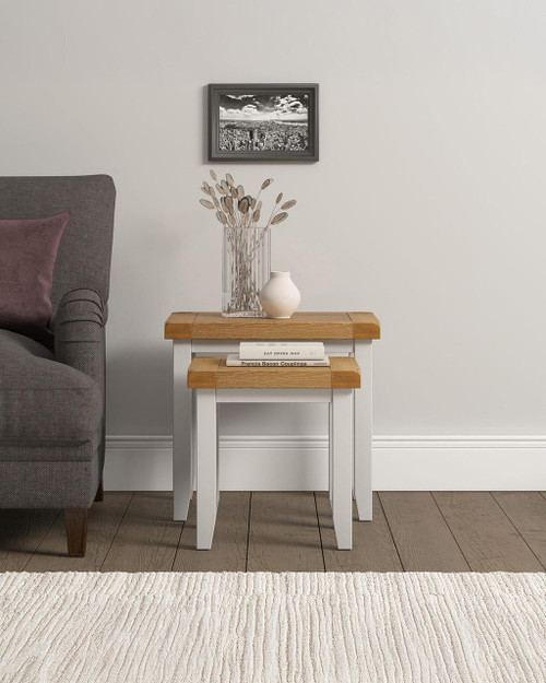 Hampton Ivory Nest of 2 Tables HI300-303-042, a set of two nested side tables with ivory and natural wood finish, placed beside a gray armchair in a cozy living room setting.