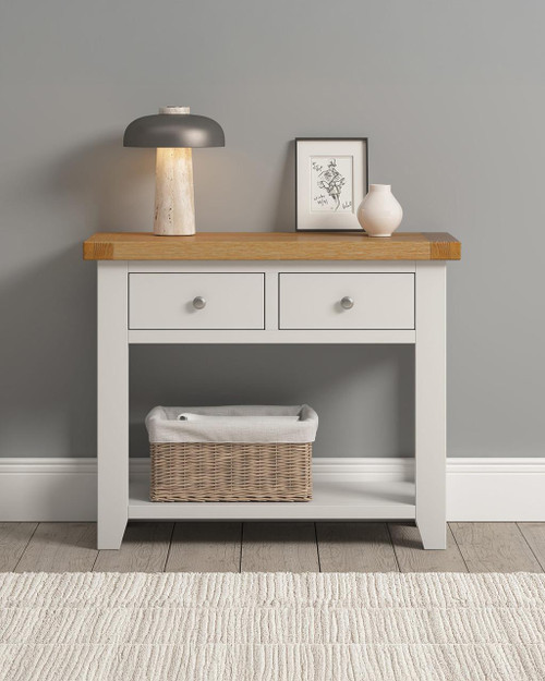Hampton Ivory 2 Drawer Console Table HI300-304-035, white wooden entryway table with two drawers, natural wood top, and lower shelf with a wicker basket, decorated with a lamp, framed art, and vase on top. Hampton Ivory 2 Drawer Console Table HI300-304-035, white wooden entryway table with two drawers, natural wood top, and lower shelf with a wicker basket, decorated with a lamp, framed art, and vase on top.