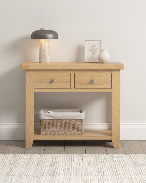 Hampton Oak 2 Drawer Console Table HO300-304-033, light oak-colored wooden console table with two drawers, lower shelf with wicker basket, modern decor with lamp, framed art, and vase on top. Hampton Oak 2 Drawer Console Table HO300-304-033, light oak-colored wooden console table with two drawers, lower shelf with wicker basket, modern decor with lamp, framed art, and vase on top.