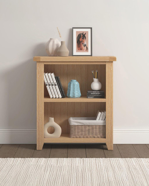 Hampton Oak Low Bookcase HO300-306-052, wooden bookcase with three shelves holding books, decorative vases, and a wicker basket, styled in a modern minimalist interior.