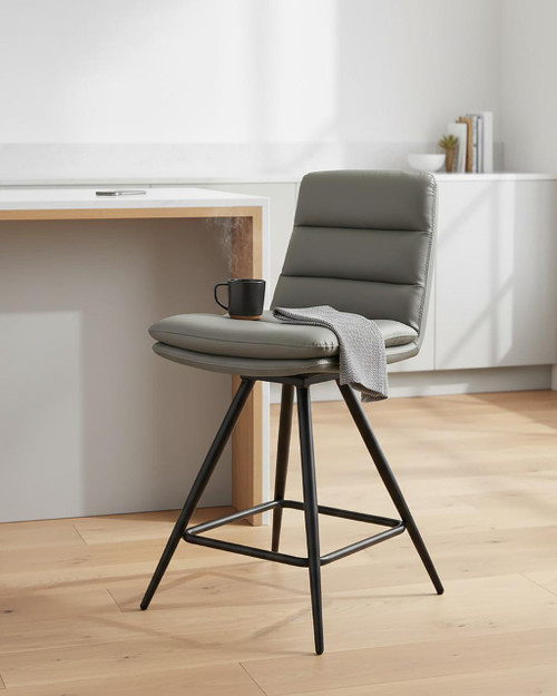 Hamilton Swivel Counter Chair in Taupe, modern padded leather seat with backrest on black metal legs, placed in a minimalist kitchen setting with a coffee mug and a gray towel on the seat. Hamilton Swivel Counter Chair in Taupe, modern padded leather seat with backrest on black metal legs, placed in a minimalist kitchen setting with a coffee mug and a gray towel on the seat.
