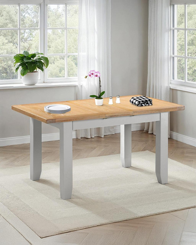 Hampton Pebble Grey Extending Dining Table HG400-403-076, modern wooden dining table with pebble grey painted legs and a natural oak top, displayed in a bright room with large windows and white curtains.