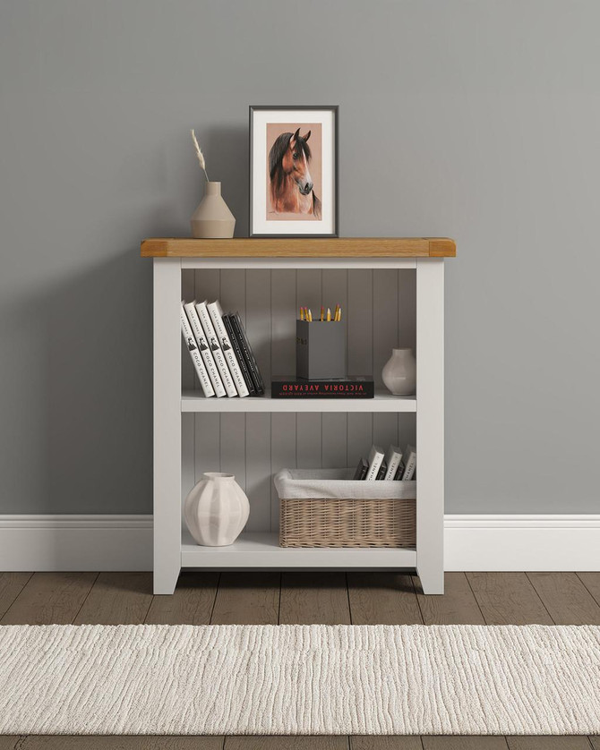 Hampton Ivory Low Bookcase HI300-306-054, an ivory painted wooden bookcase with a natural wood top, decorated with books, a basket, and vases in a room.
