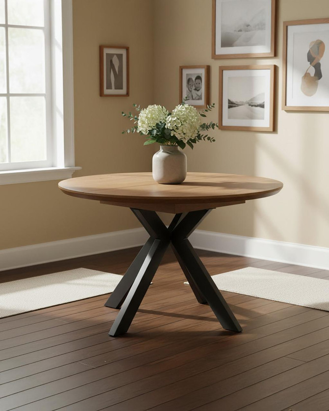 Hamilton Rustic Oak Round 120cm - 160cm Extending Table, modern round wooden dining table with a light oak finish and black angled metal legs, decorated with a white flower vase in a stylish dining room.