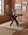 Hamilton Black Ash Round 120cm - 160cm Extending Table, black wooden round dining table with crisscross legs in a cozy room with pink walls and framed artwork.