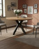 Hamilton Rustic Oak 120cm Round Table, wooden dining table with a round top and black X-shaped legs, decorated with a vase of white flowers in a modern dining room.