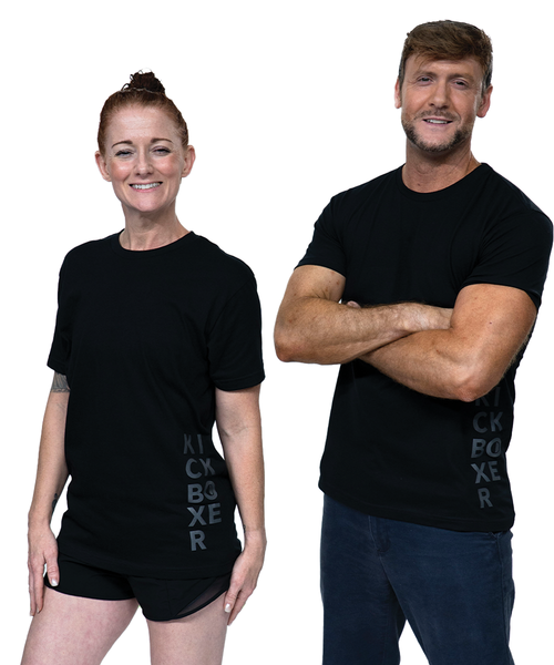 A man with a black shirt on arms crossed standing next to a woman in the same black shirt with her hair up in a bun and smiling toward the camera