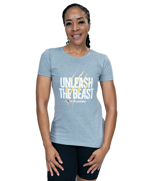 A woman smiling at the camera in grey women’s cut t-shirt that say "unleash the beast" in white text with yellow claw mark design behind it and an I Love Kickboxing logo underneath