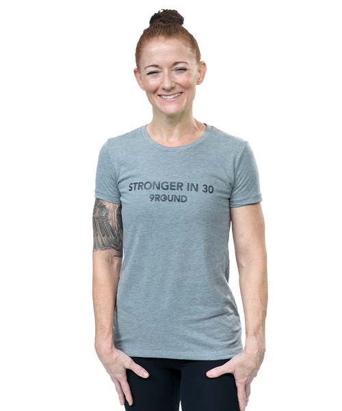 A woman in a grey t-shirt with her hair in a bun. The shirt reads, "Stronger in 30 9Round"