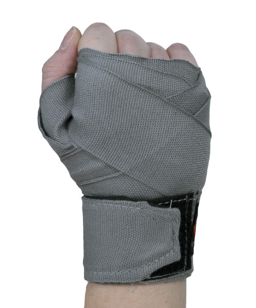 A hand held in the air in a fist with the back of the hand facing you and wearing a grey boxing hand wrap