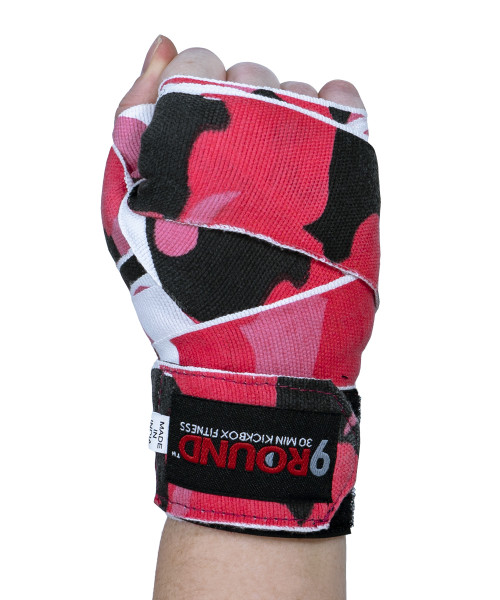 A hand held in the air in a fist with the back of the hand facing you and wearing a pink camo pattern boxing hand wrap