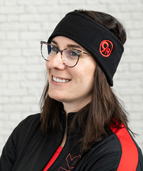 A photo of a young adult woman with glasses wearing a black fleece headband with a red 9Round circle logo off to one side