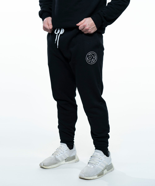 A bottom view of a pair of black joggers or sweatpants on a young adult male with a white circle 9Round logo