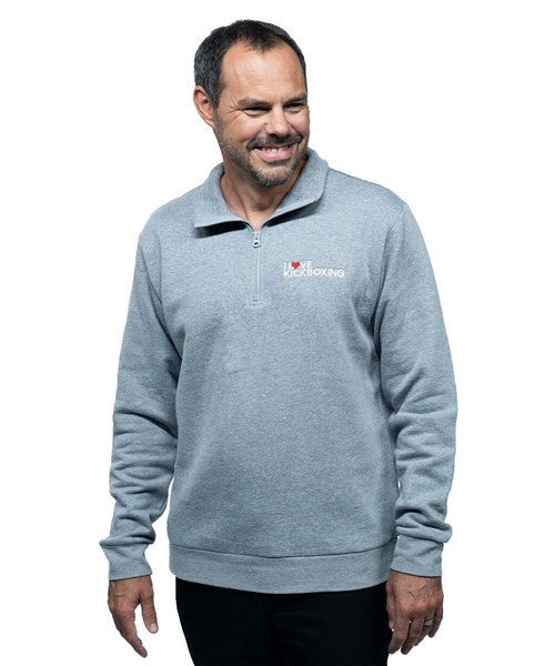 A man wearing a gray quarter-zip sweatshirt with the I Love Kickboxing logo on the left chest, standing and smiling against a white background.