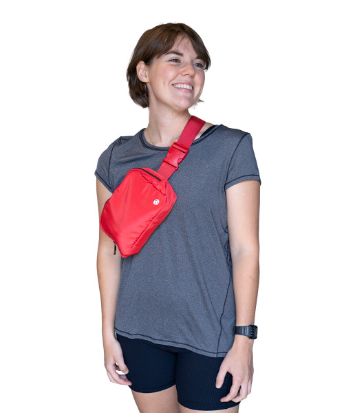 A young woman wearing a grey t-shirt with a bright red belt bag across her chest