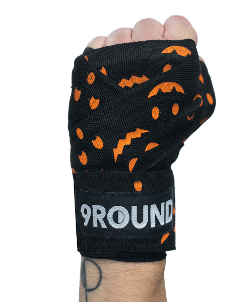 A Halloween-themed pair of boxing hand wraps by 9Round featuring a black base with assorted orange pumpkin faces.