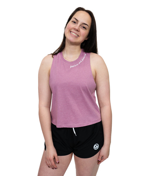 Woman standing and smiling, wearing a sleeveless pink top and black shorts with a white logo, against a plain white background.