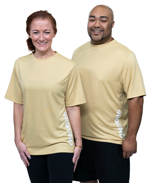 Two people wearing light gold 9Round athletic shirts and black shorts stand side by side, smiling at the camera against a white background.