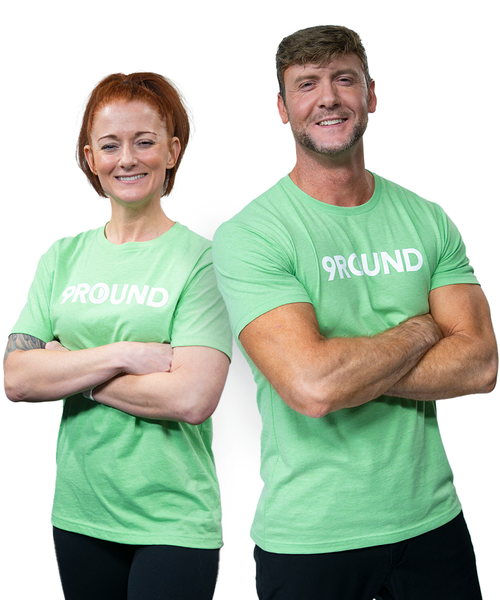 Two people wearing matching light green 9ROUND t-shirts stand side by side with arms crossed, smiling at the camera against a plain white background.