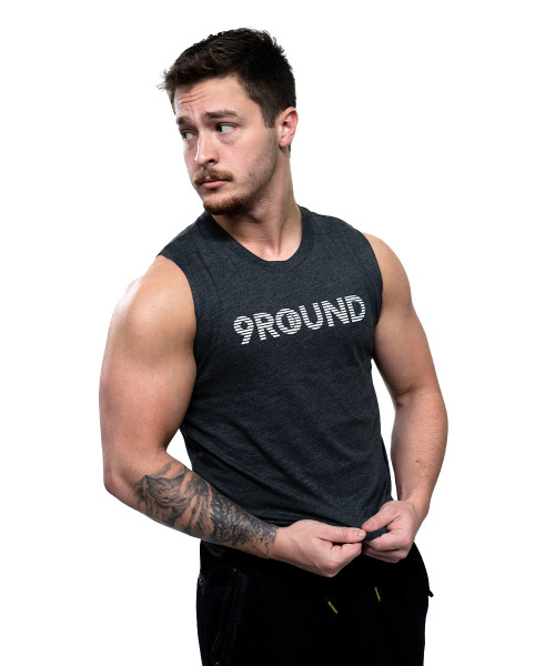 A man with a mustache and arm tattoo wears a sleeveless 9ROUND shirt, looking to the side against a plain white background.
